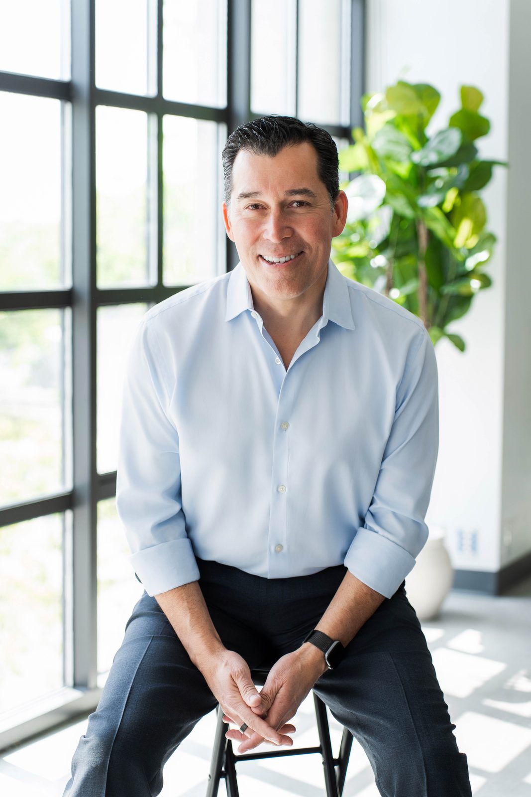 John Abril smiling, seated in a light blue shirt at his Ontario office