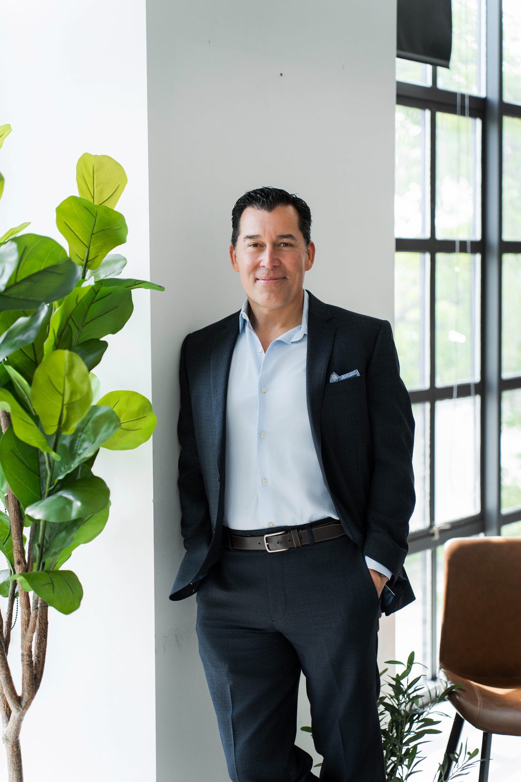 John Abril leaning by the window in a navy suit at his Ontario office