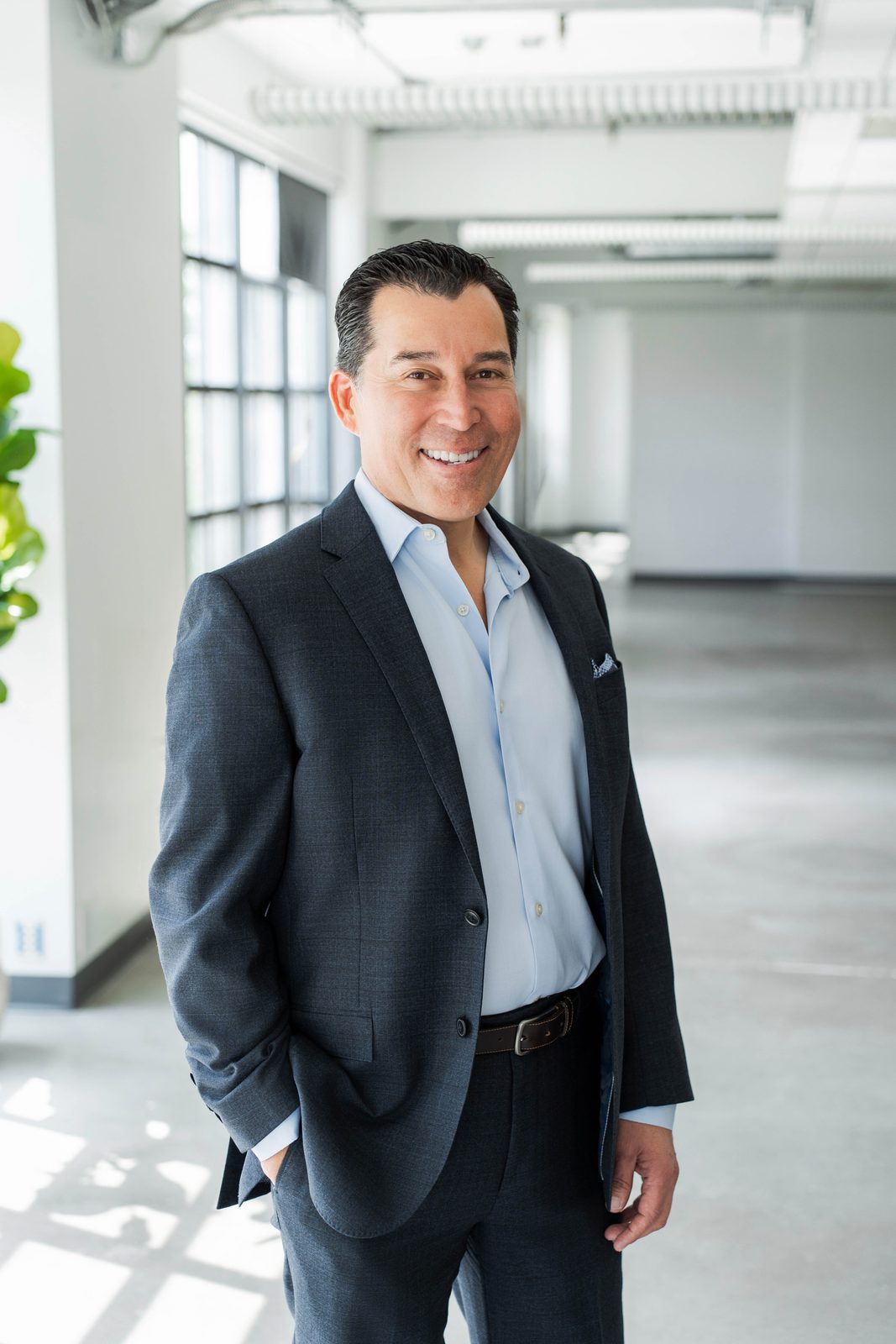 John Abril smiling in a navy suit at his Ontario office